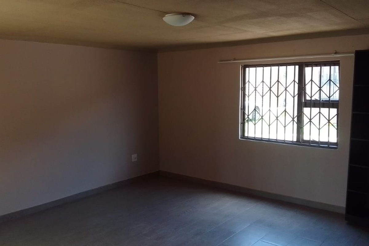 An empty living room featuring tiled flooring and a window fitted with a security gate.