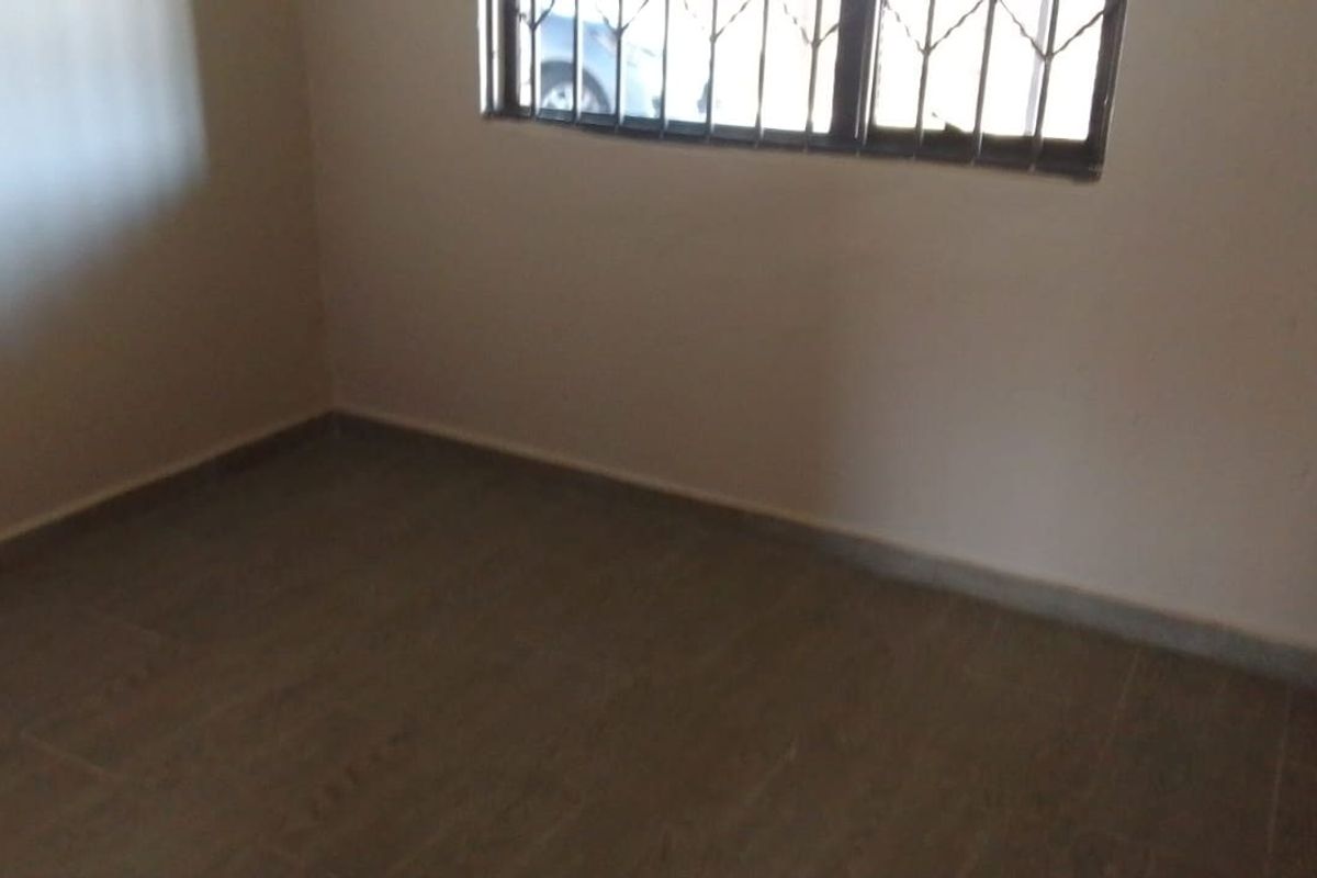An empty bedroom featuring tiled flooring and a window fitted with security bars.