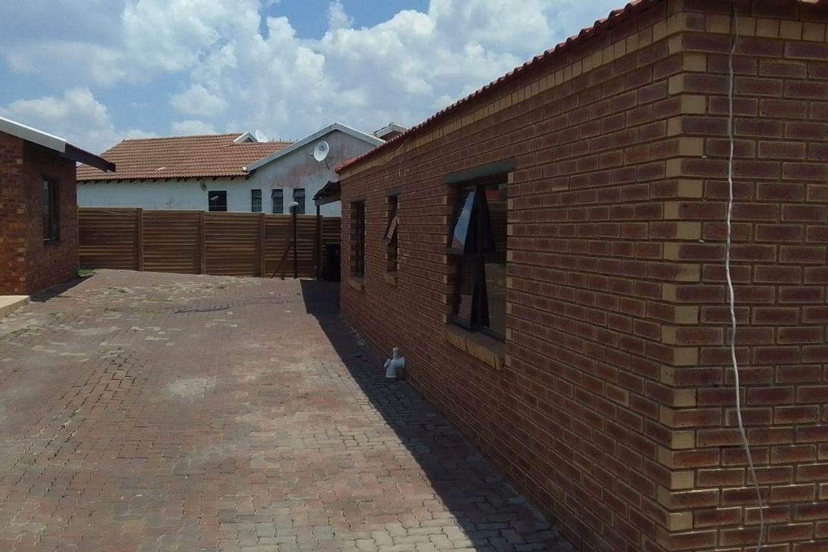 Rear exterior view of the property featuring face brick walls, a paved courtyard area, and tiled roofing.
