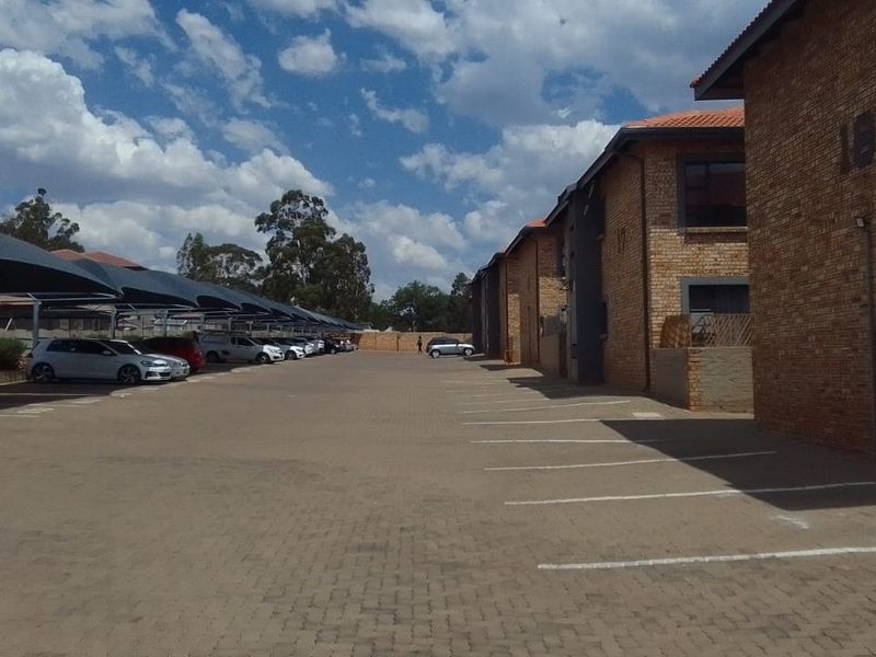 Exterior view of the apartment complex featuring a paved parking area with shade cloth carports and facebrick building facades.