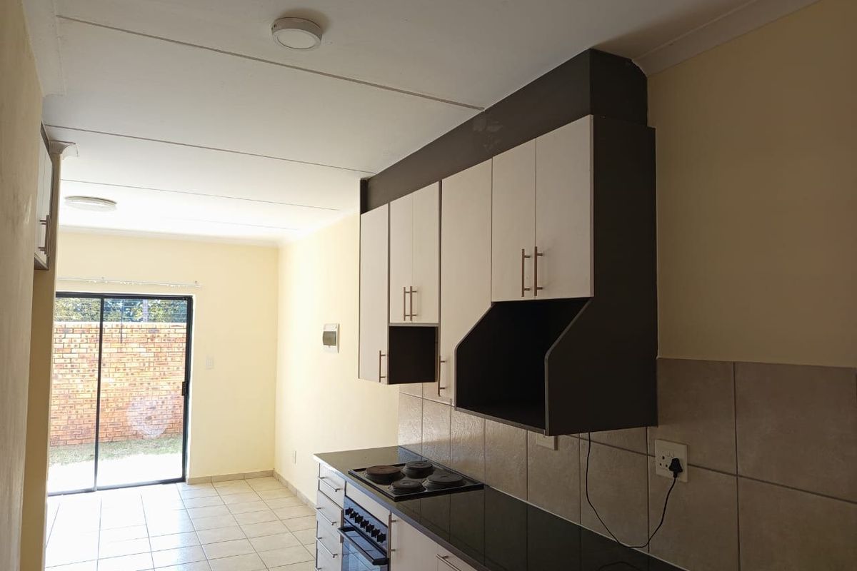 A clean, functional kitchen featuring built-in cabinetry, granite countertops, an electric hob, and an oven, with direct access to an outdoor area.