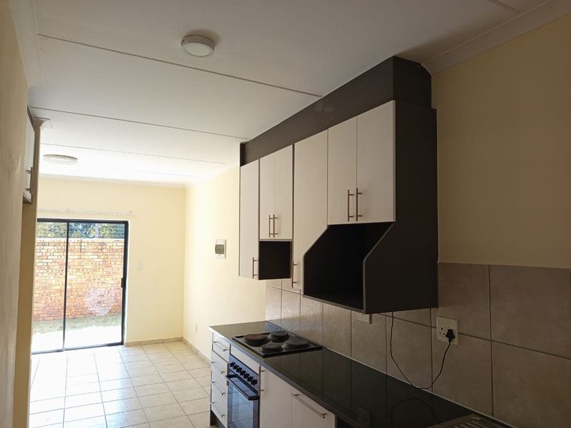 A clean, functional kitchen featuring built-in cabinetry, granite countertops, an electric hob, and an oven, with direct access to an outdoor area.