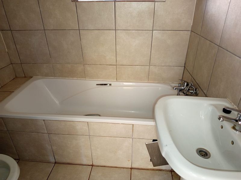 A functional bathroom featuring a built-in bathtub and a pedestal washbasin with neutral ceramic tiling throughout.