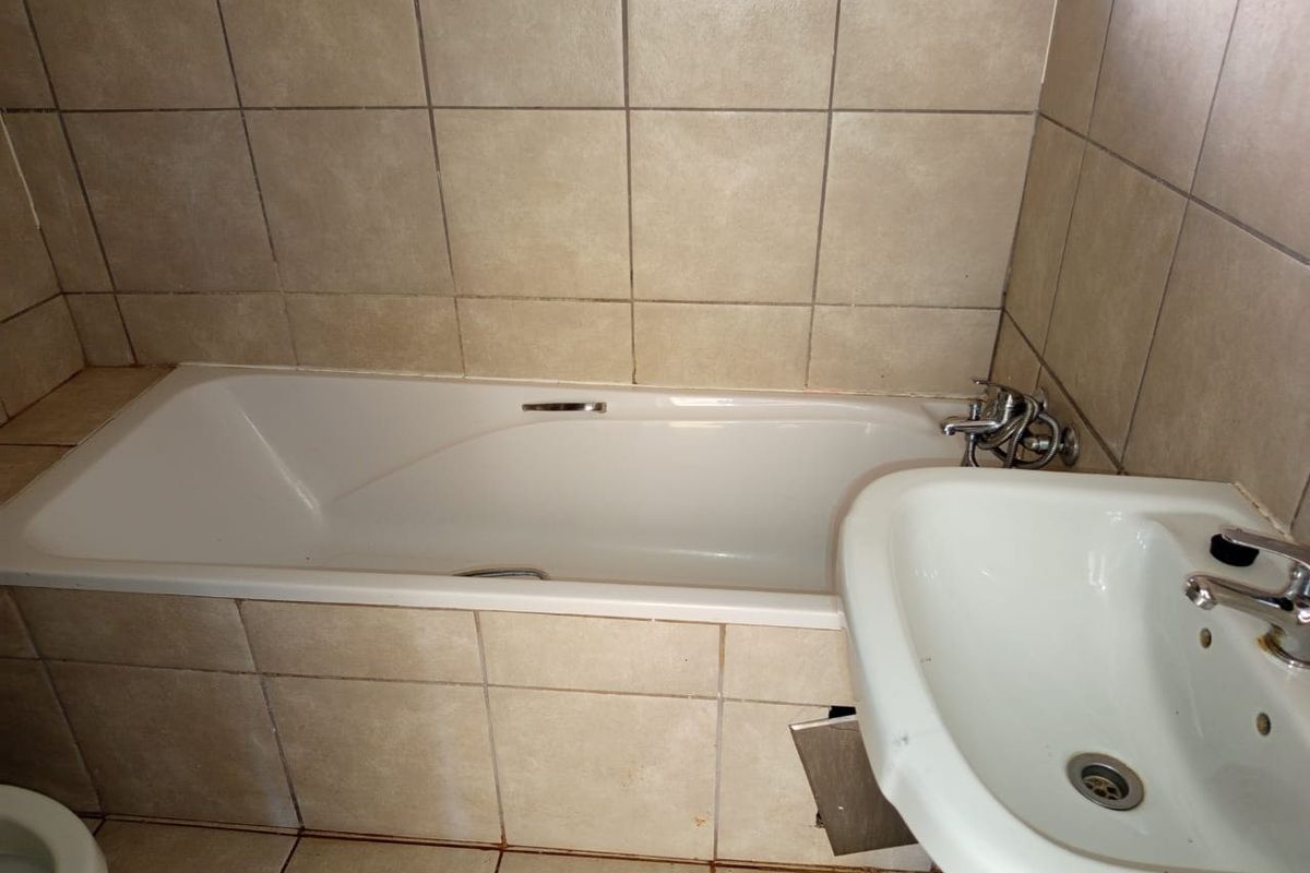 A functional bathroom featuring a built-in bathtub and a pedestal washbasin with neutral ceramic tiling throughout.