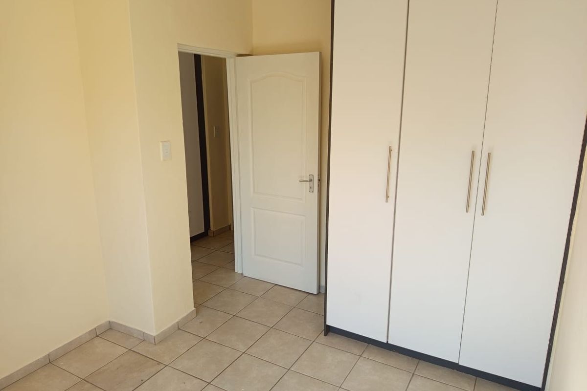 A clean, empty bedroom featuring neutral tiled flooring and a large built-in wardrobe with modern handles.