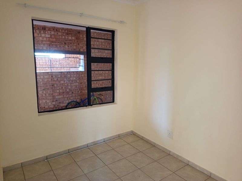 An empty bedroom featuring neutral tiled flooring and a black metal window frame, offering a clean and versatile space ready for personalization.