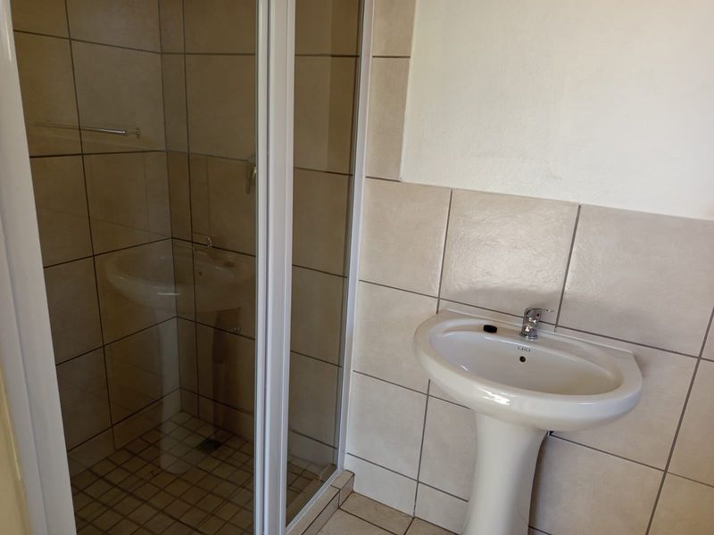 A functional bathroom featuring a pedestal basin, chrome mixer tap, and a glass-enclosed shower with neutral wall and floor tiling.