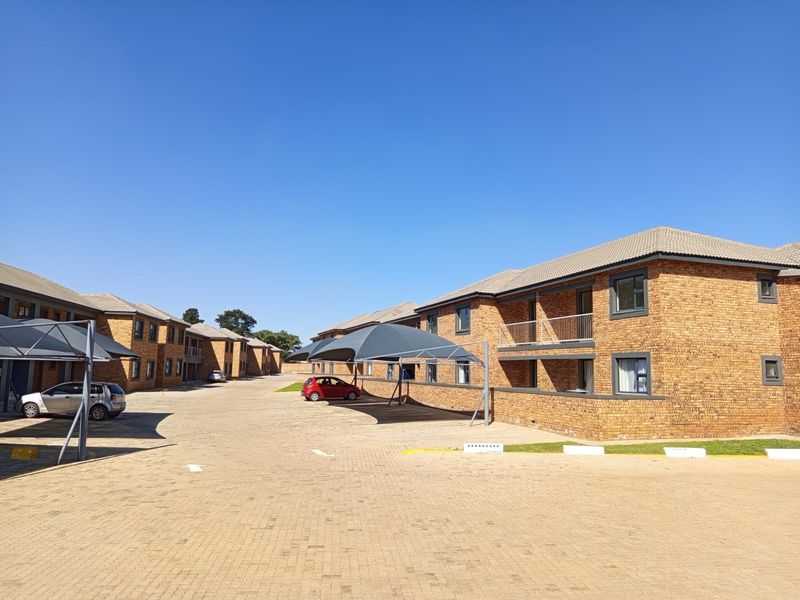 Exterior view of a multi-unit apartment complex featuring face brick construction, tiled roofs, paved parking areas, and covered carport structures.