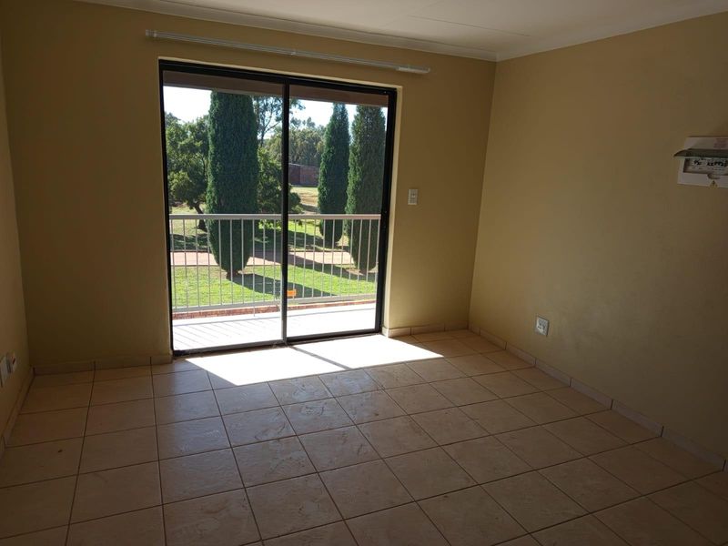 An empty living room featuring ceramic tile flooring and a sliding glass door that provides access to a balcony with garden views.