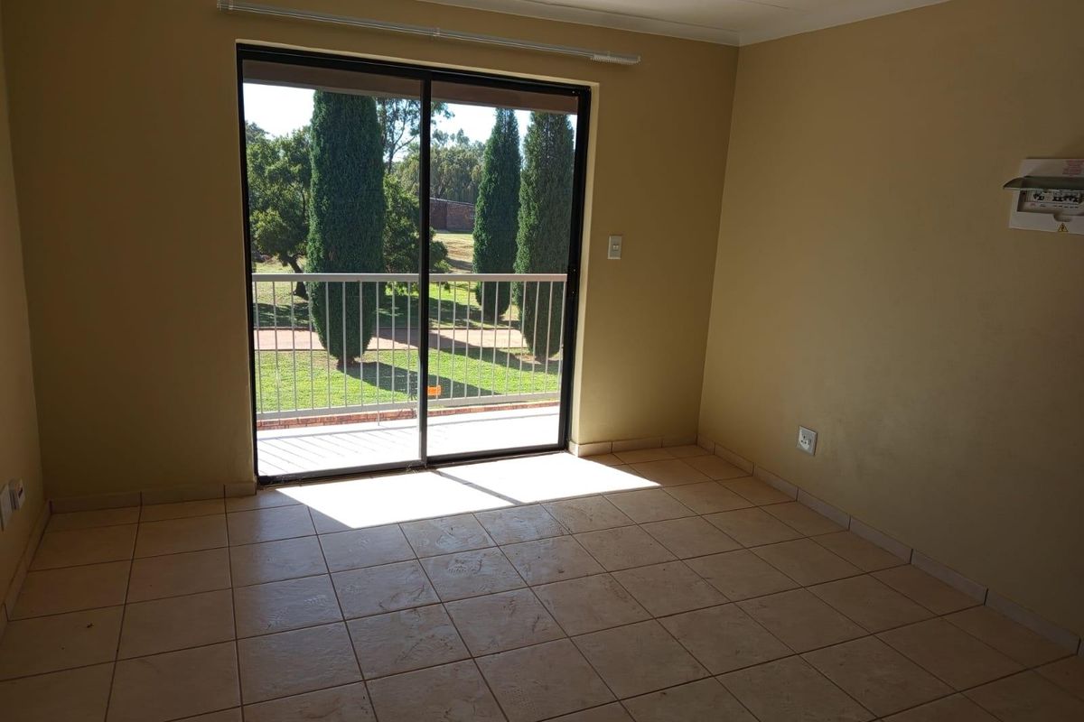 An empty living room featuring ceramic tile flooring and a sliding glass door that provides access to a balcony with garden views.