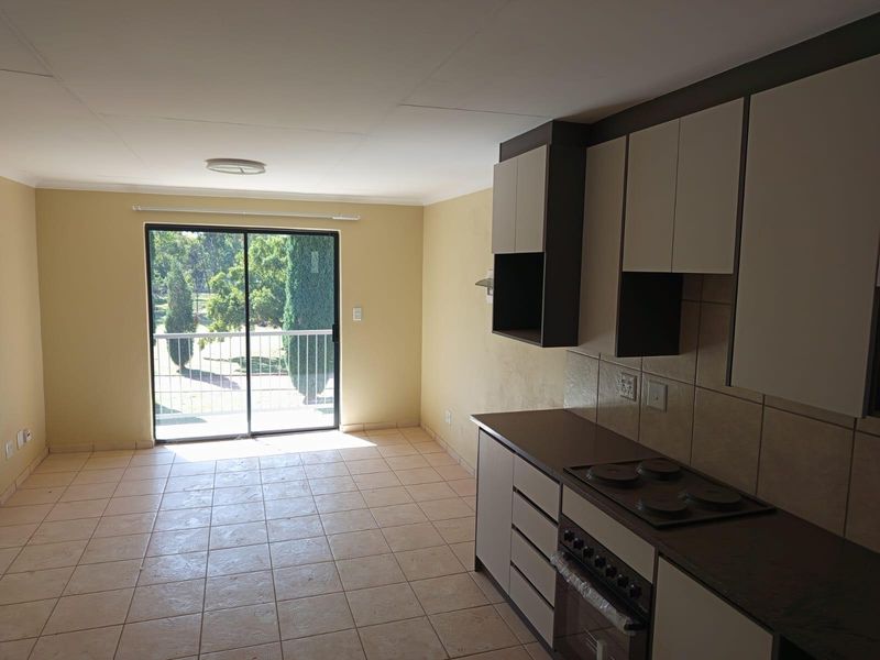 Open-plan kitchen and living area featuring tiled floors, built-in cabinetry with an integrated stove, and a sliding door leading to a balcony.