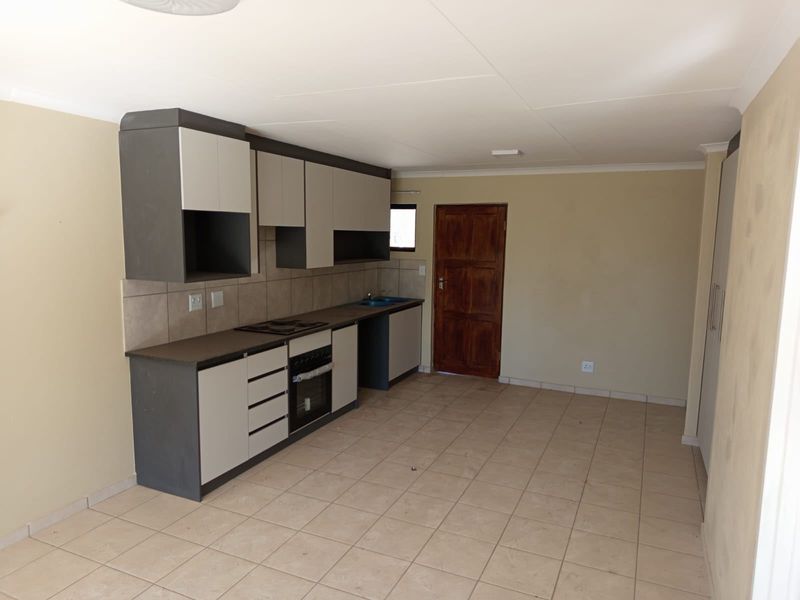 An open-plan kitchen area featuring modern two-tone cabinetry, built-in oven and hob, tiled flooring, and neutral wall finishes in a vacant space.