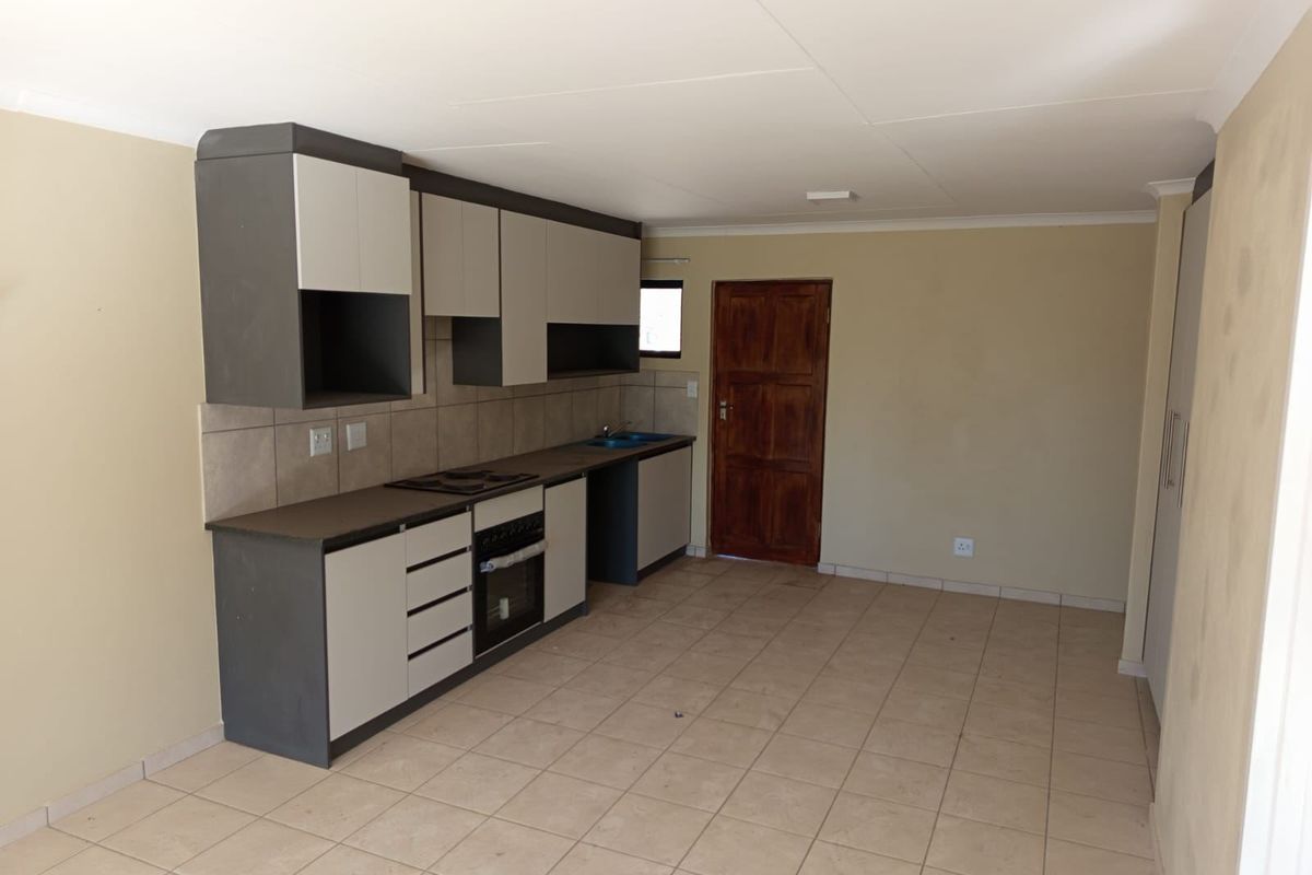 An open-plan kitchen area featuring modern two-tone cabinetry, built-in oven and hob, tiled flooring, and neutral wall finishes in a vacant space.