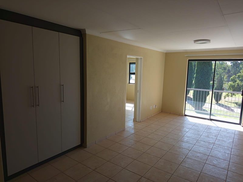 An empty bedroom featuring tiled flooring, built-in cupboards, and a sliding glass door providing access to a balcony with exterior views.
