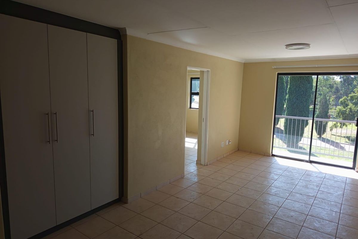 An empty bedroom featuring tiled flooring, built-in cupboards, and a sliding glass door providing access to a balcony with exterior views.