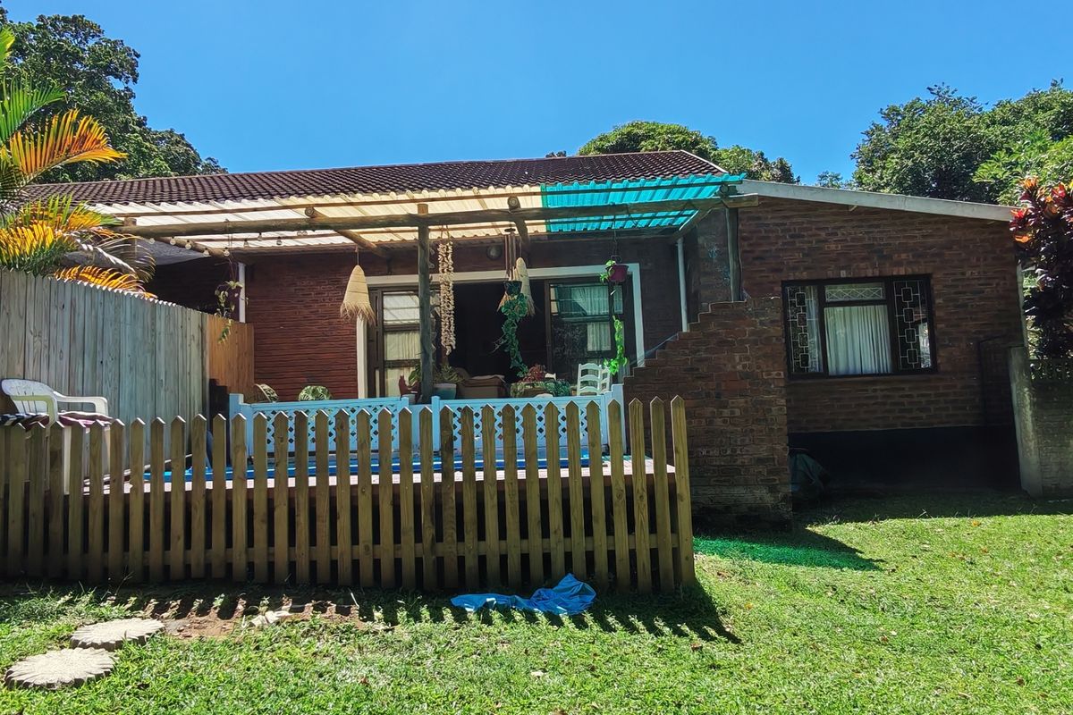 Rear view of the house featuring a brick facade, a covered patio area, and a timber picket fence overlooking the garden.