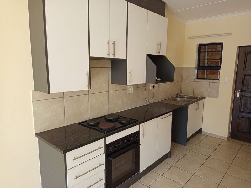 A functional kitchen featuring built-in cabinetry, granite countertops, an integrated electric hob and oven, and a double sink with tiled backsplash.