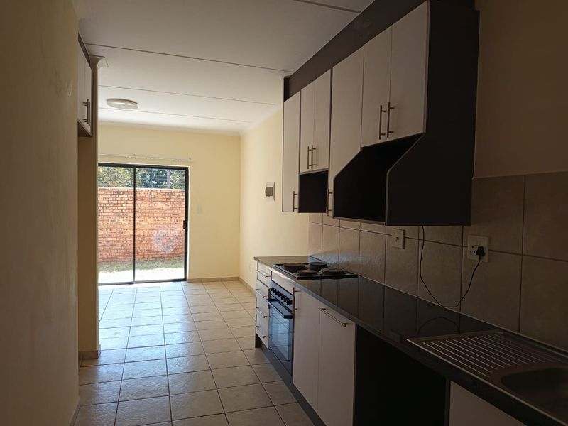 A functional kitchen featuring built-in cabinetry, an electric hob, oven, and tiled splashback, leading directly to an outdoor area through a sliding glass door.