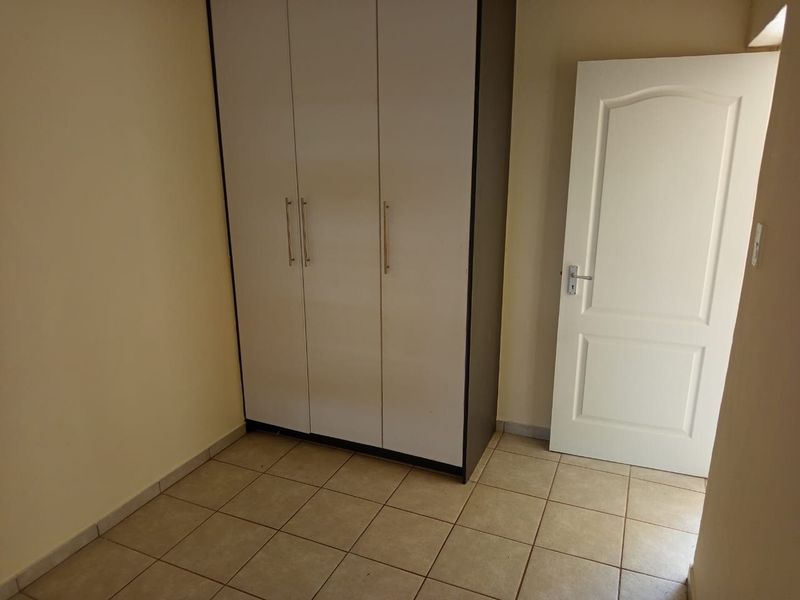 A clean, empty bedroom featuring neutral tiled flooring and a built-in wardrobe with white doors.