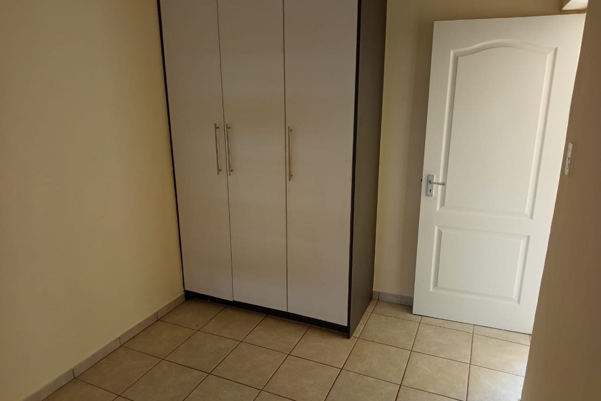 A clean, empty bedroom featuring neutral tiled flooring and a built-in wardrobe with white doors.