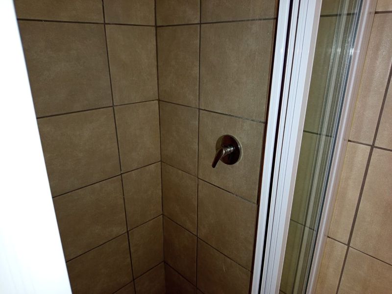 A compact shower stall featuring brown wall tiles and a standard chrome shower mixer tap.