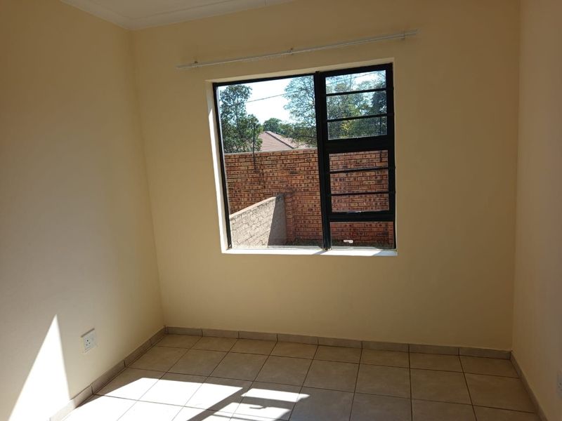 A bright, empty bedroom featuring neutral wall paint, tiled flooring, and an aluminium window with security bars overlooking the rear exterior.