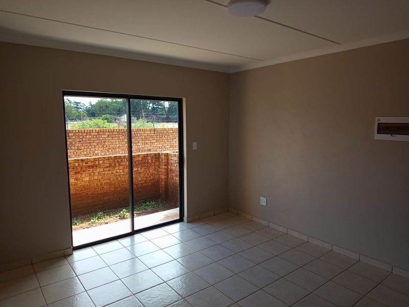 An empty living room featuring neutral walls, ceramic floor tiles, and a sliding glass door providing access to a private outdoor area.