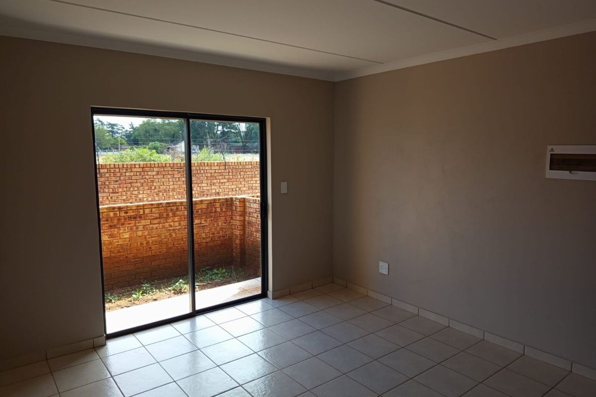 An empty living room featuring neutral walls, ceramic floor tiles, and a sliding glass door providing access to a private outdoor area.