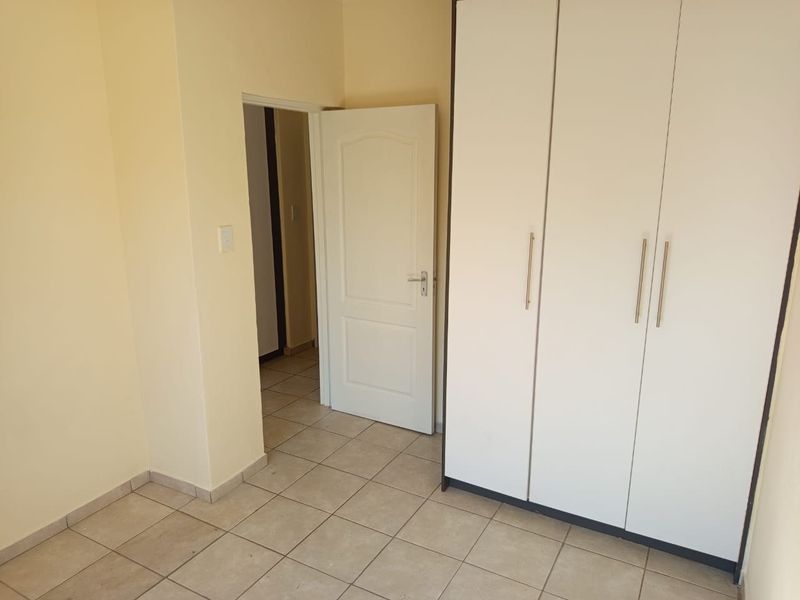 A clean, empty bedroom featuring neutral tiled flooring and a large built-in wardrobe with modern handles.