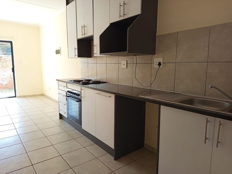 A clean, functional kitchen featuring modern two-tone cabinetry, granite countertops, a built-in oven and hob, and neutral tiled flooring.