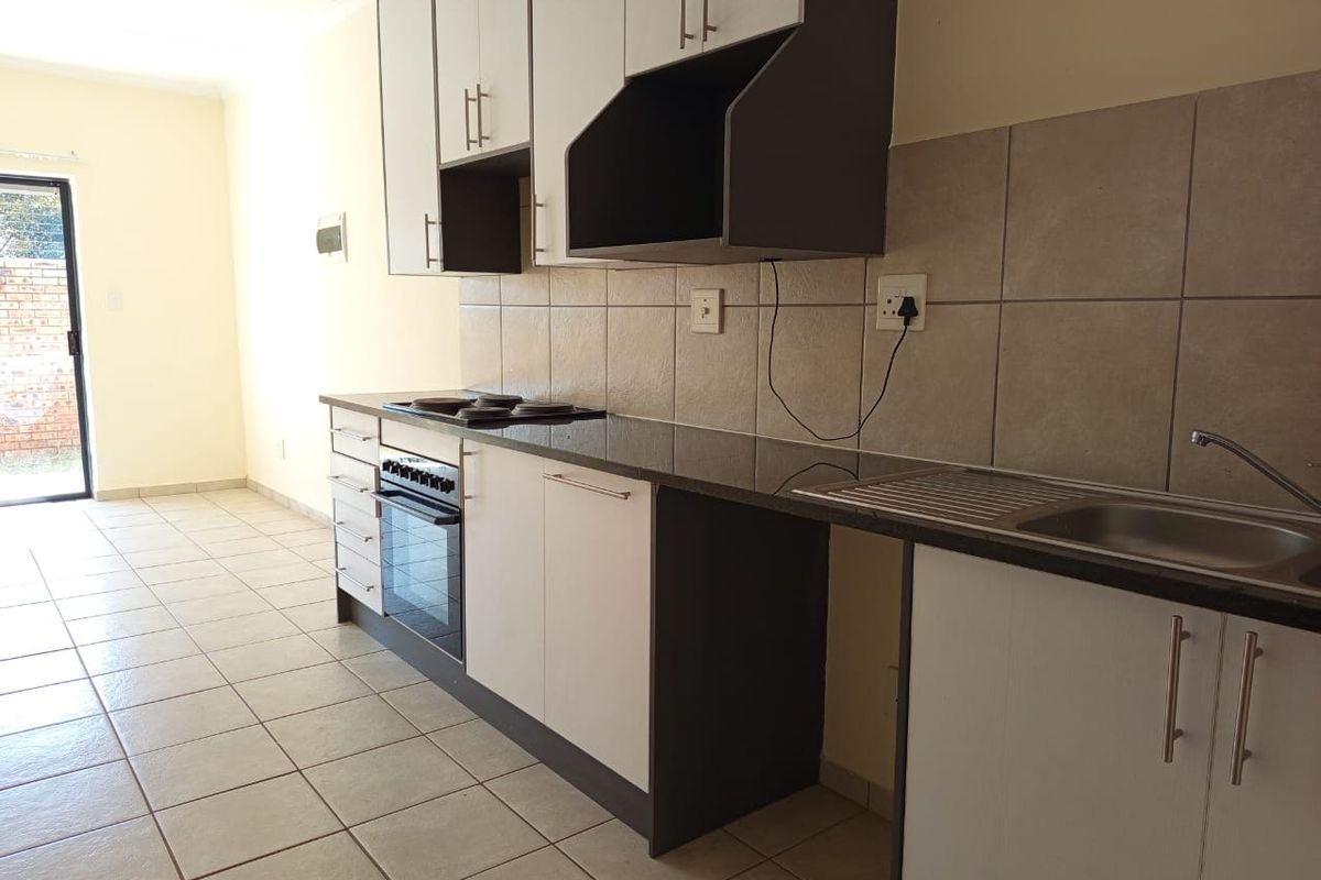 A clean, functional kitchen featuring modern two-tone cabinetry, granite countertops, a built-in oven and hob, and neutral tiled flooring.