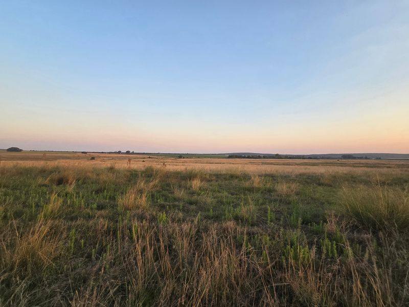 Expansive open farmland landscape featuring natural grasslands under a clear sunset sky.