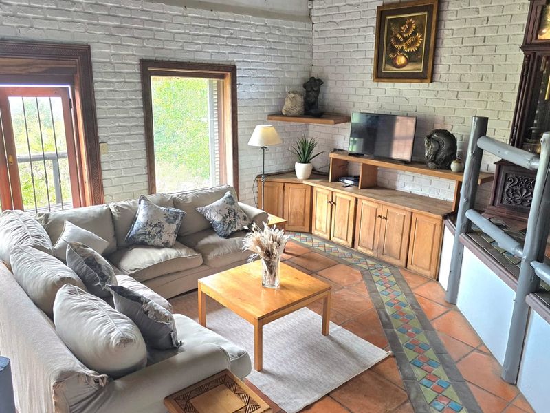 A cozy living room featuring white-painted exposed brick walls, traditional terracotta tile flooring with decorative inlay, and a built-in fireplace with wooden cabinetry.