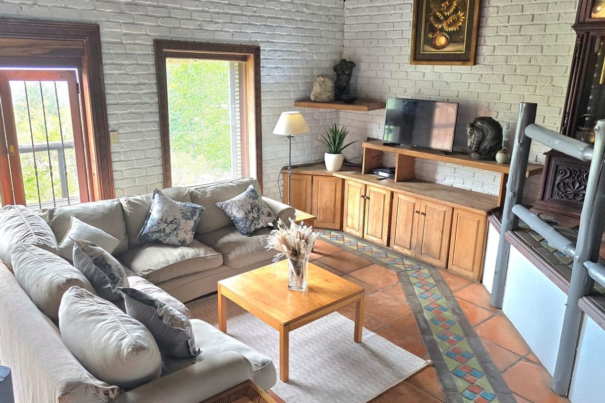 A cozy living room featuring white-painted exposed brick walls, traditional terracotta tile flooring with decorative inlay, and a built-in fireplace with wooden cabinetry.