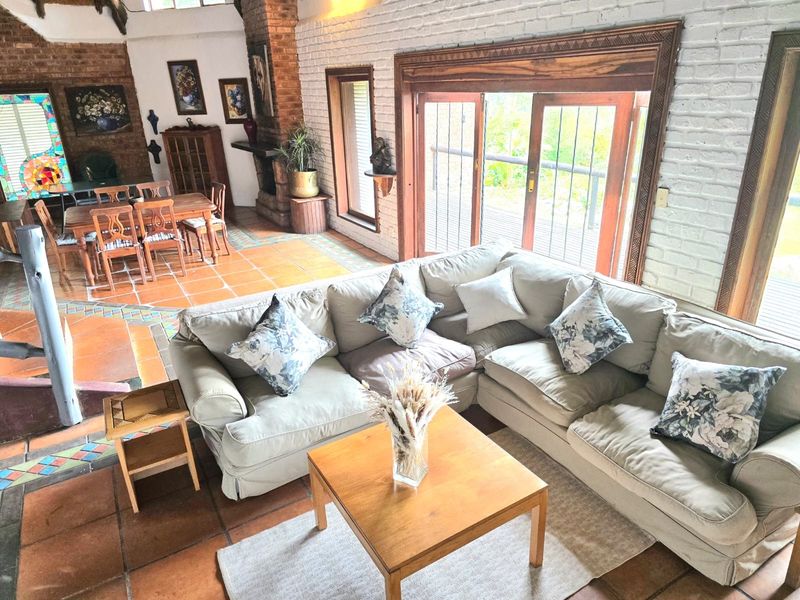 Spacious open-plan living and dining area featuring terracotta tile flooring, exposed brick fireplace, and large wooden doors opening to the outdoors.