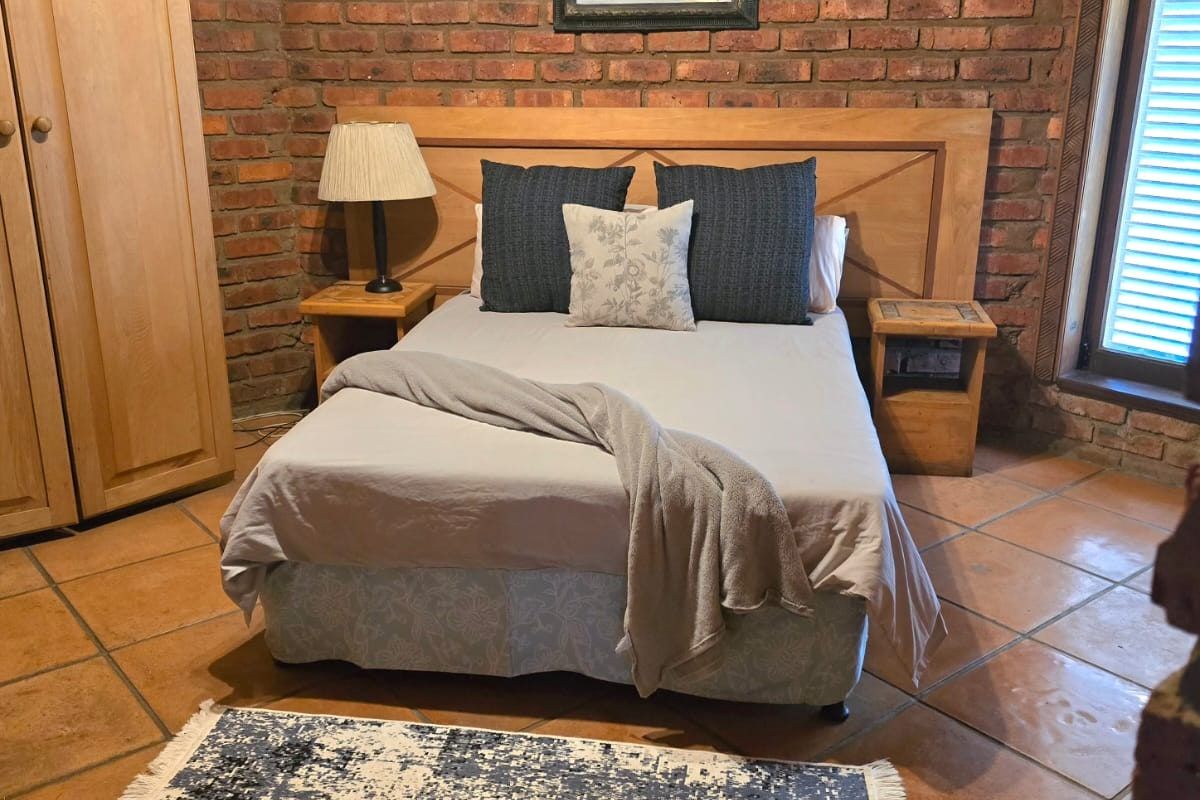 A rustic bedroom featuring exposed brick walls, terracotta floor tiles, and a built-in wooden wardrobe, offering a warm and traditional aesthetic.