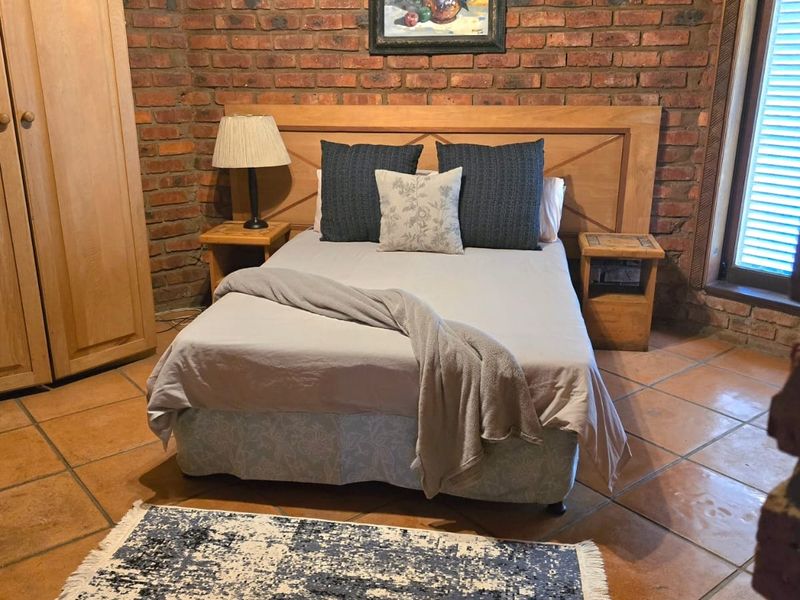 A rustic bedroom featuring exposed brick walls, terracotta floor tiles, and a built-in wooden wardrobe, offering a warm and traditional aesthetic.