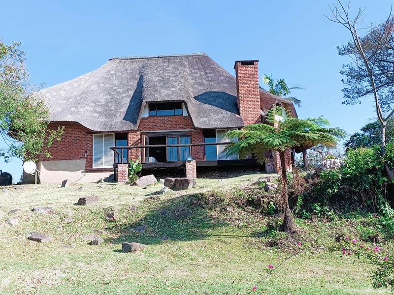 Rear view of a traditional brick house featuring a thatched roof, a prominent brick chimney, and a raised timber deck overlooking the garden.