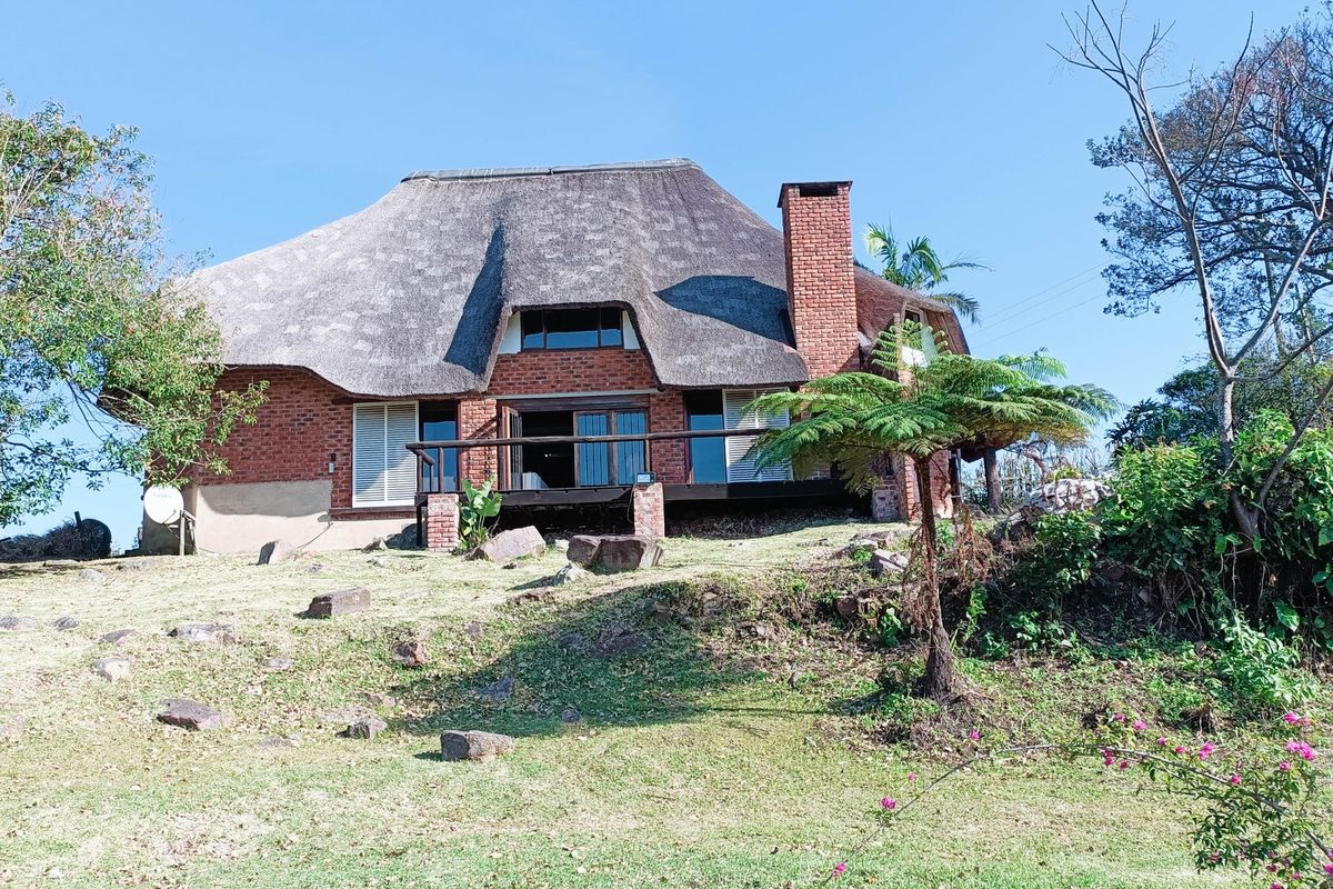 Rear view of a traditional brick house featuring a thatched roof, a prominent brick chimney, and a raised timber deck overlooking the garden.