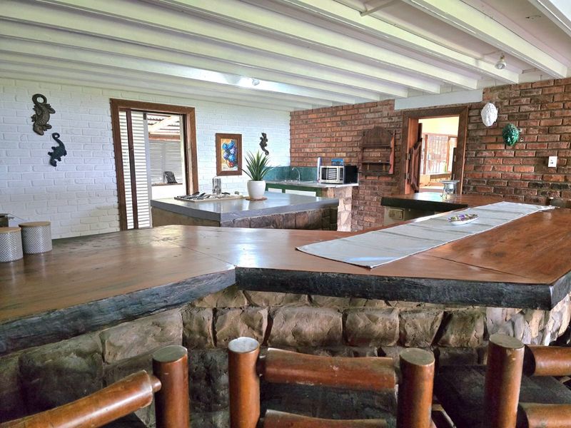 Rustic bar area featuring a stone-clad counter with a timber top, exposed brick walls, and exposed beam ceilings, offering a unique entertainment space.