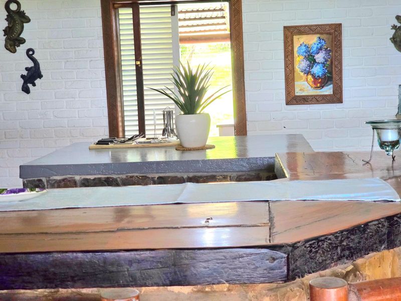 A rustic indoor bar area featuring a solid timber counter, painted brick walls, and a window with louvre shutters.