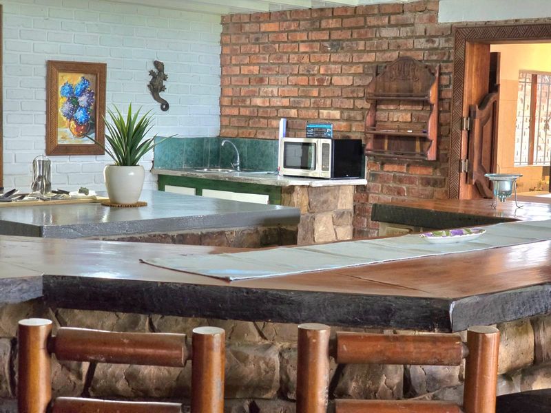 A rustic bar area featuring a stone-clad counter with a timber top, exposed brick walls, and a built-in sink with tiled splashback.