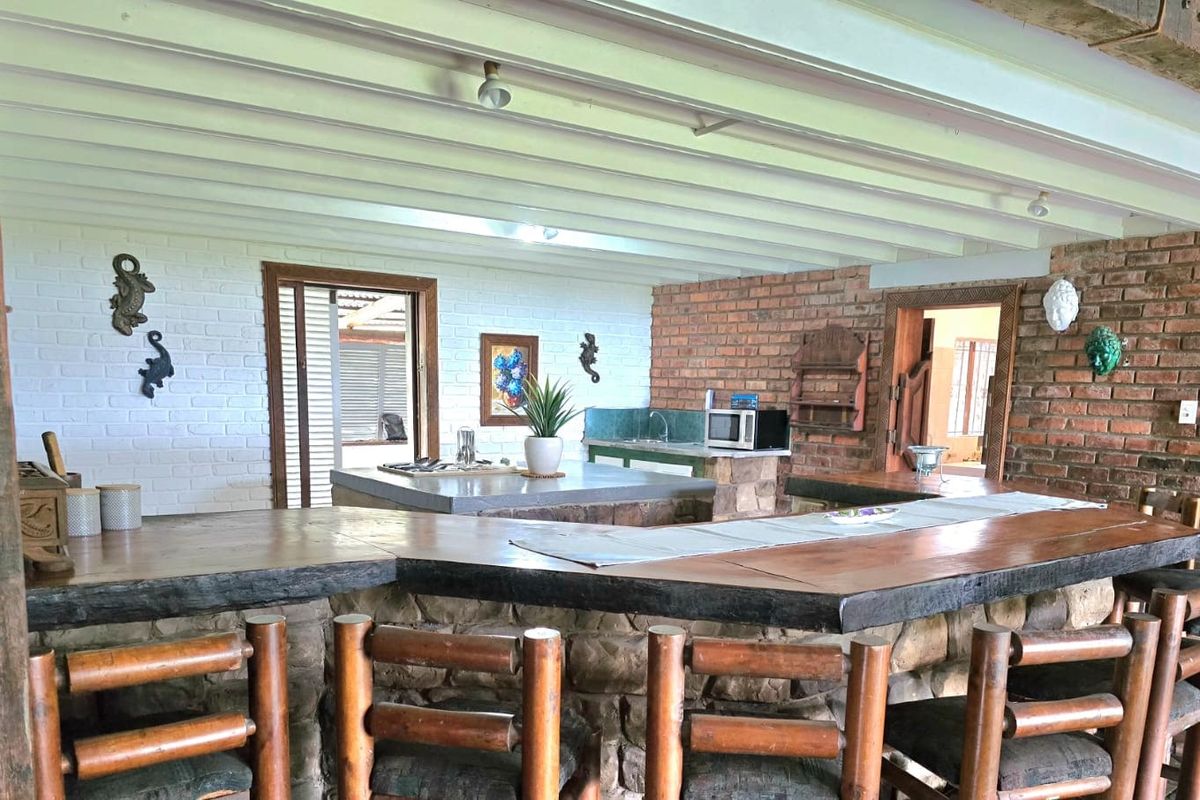 Rustic kitchen featuring a large stone-clad breakfast bar with timber countertop, exposed beam ceiling, and brick feature walls.