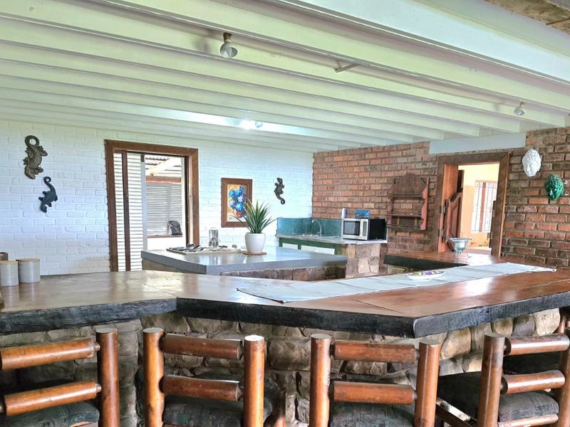 Rustic kitchen featuring a large stone-clad breakfast bar with timber countertop, exposed beam ceiling, and brick feature walls.