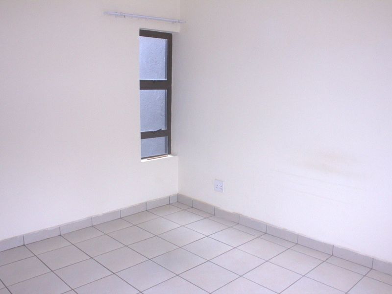 A clean, empty bedroom featuring neutral tiled flooring, a single aluminium window, and a fitted curtain rail, ready for personalization.