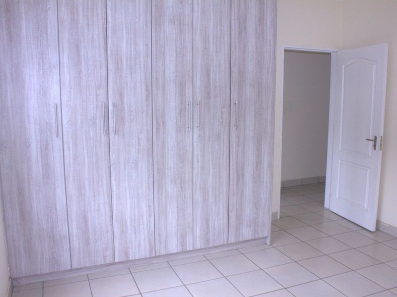 A clean, empty bedroom featuring light wood-grain built-in cupboards and neutral floor tiles, offering a versatile space ready for personalization.