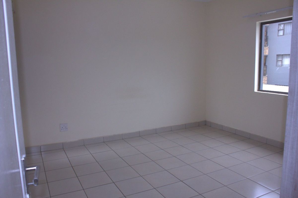 A clean, empty bedroom featuring neutral tiled flooring, plain walls, and a window providing natural light.