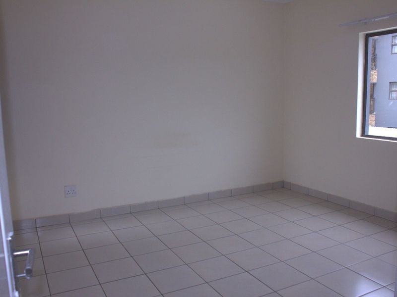 A clean, empty bedroom featuring neutral tiled flooring, plain walls, and a window providing natural light.