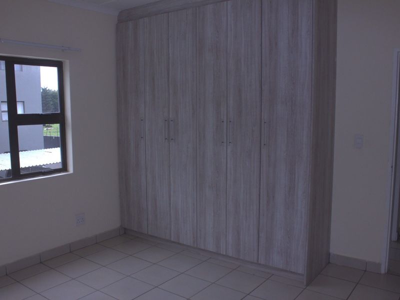 A clean, empty bedroom featuring modern light wood-finish built-in cupboards and neutral tiled flooring.