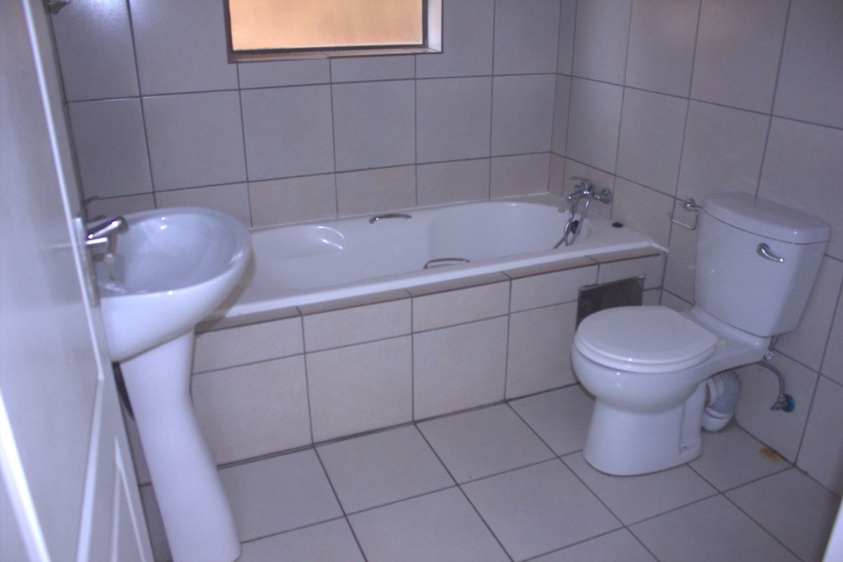 A functional bathroom featuring a pedestal basin, a built-in bathtub, and a toilet, finished with neutral ceramic wall and floor tiles.